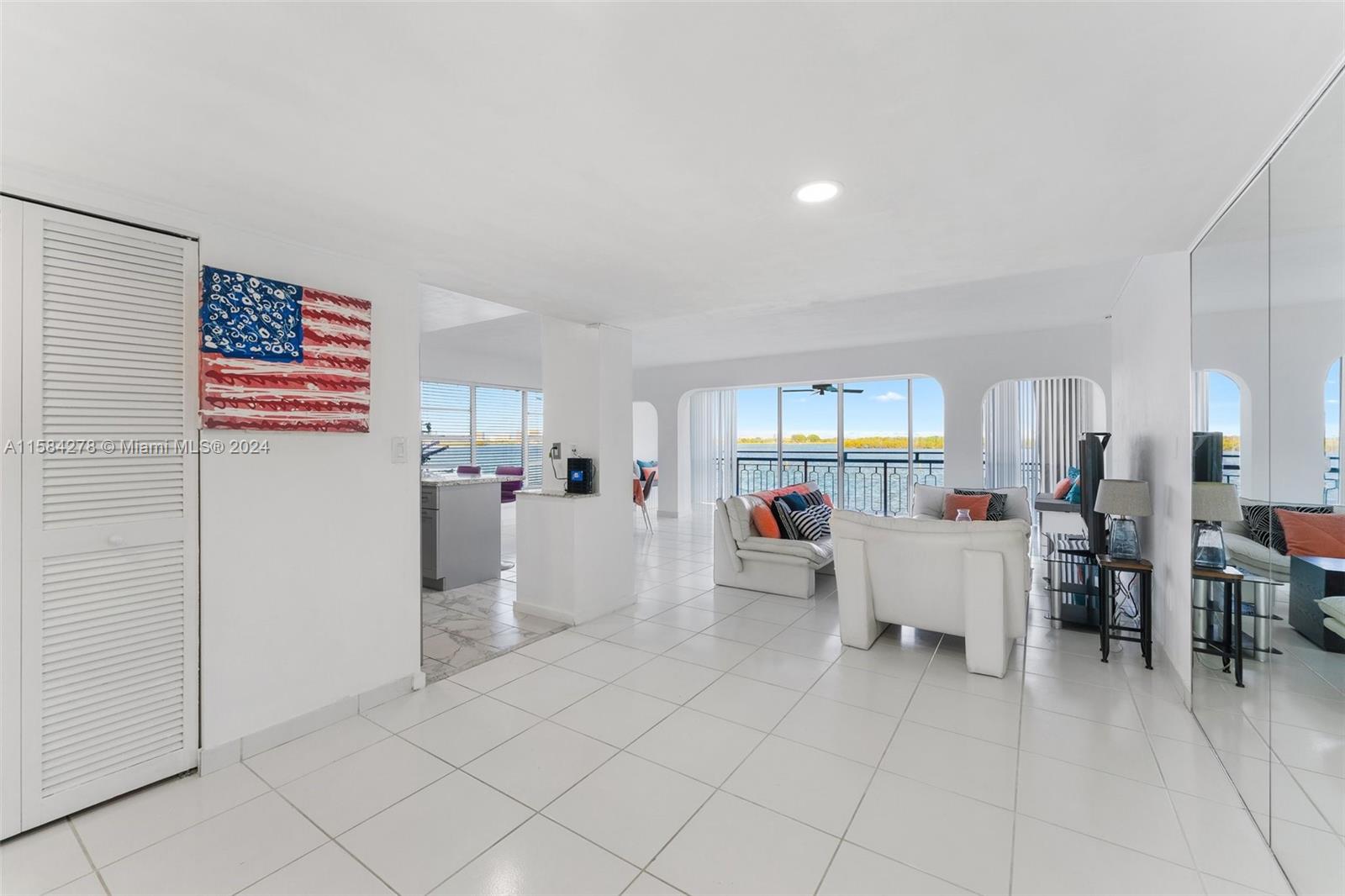 A bright living room features white tile floors, a balcony with water views, and mirrored walls — 11111 Biscayne Blvd # 3A, Miami FL 33181, MIAMI, FL