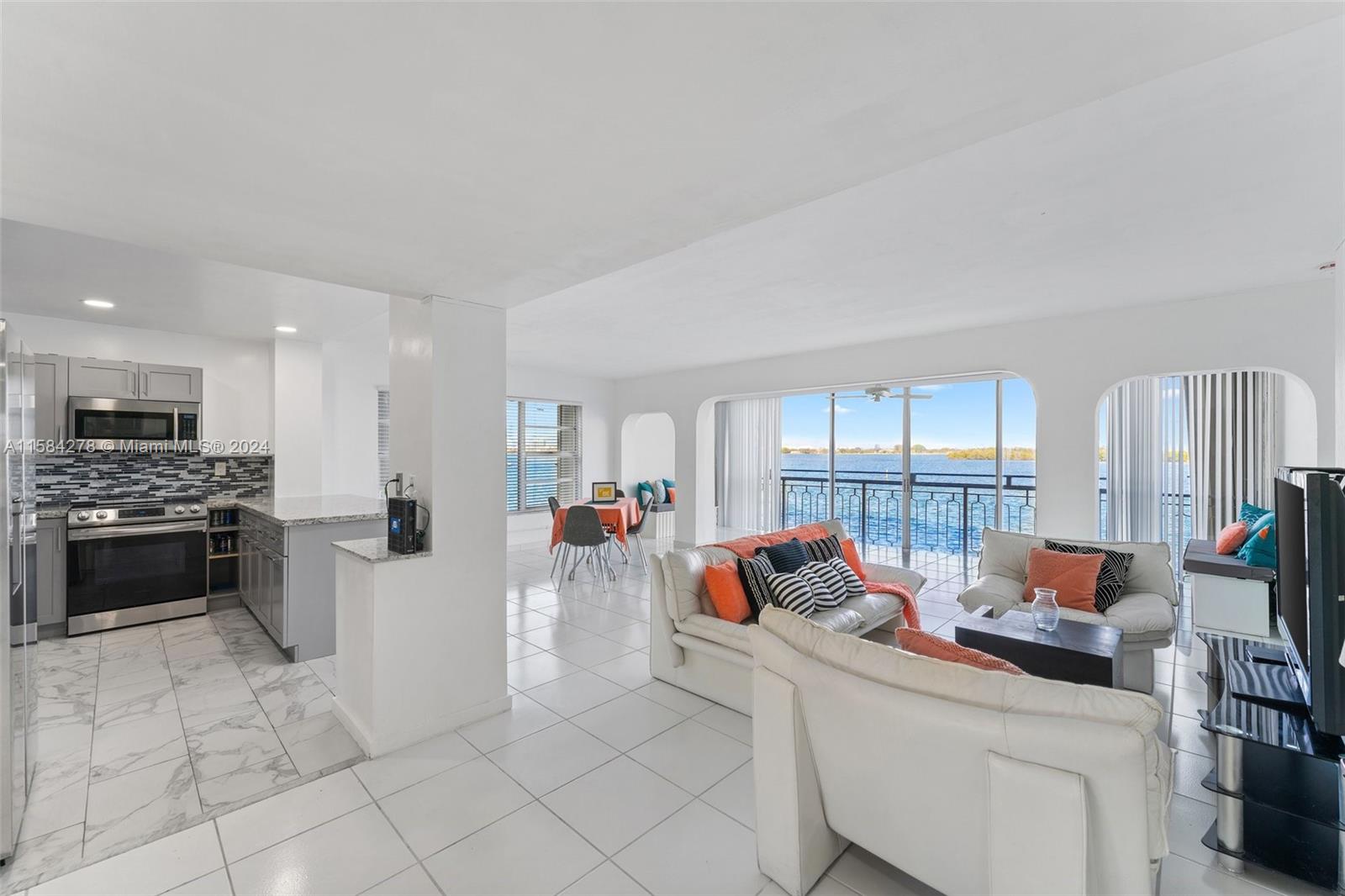 An open-concept living area and kitchen with white tile floors and a waterfront balcony view — 11111 Biscayne Blvd # 3A, Miami FL 33181, MIAMI, FL