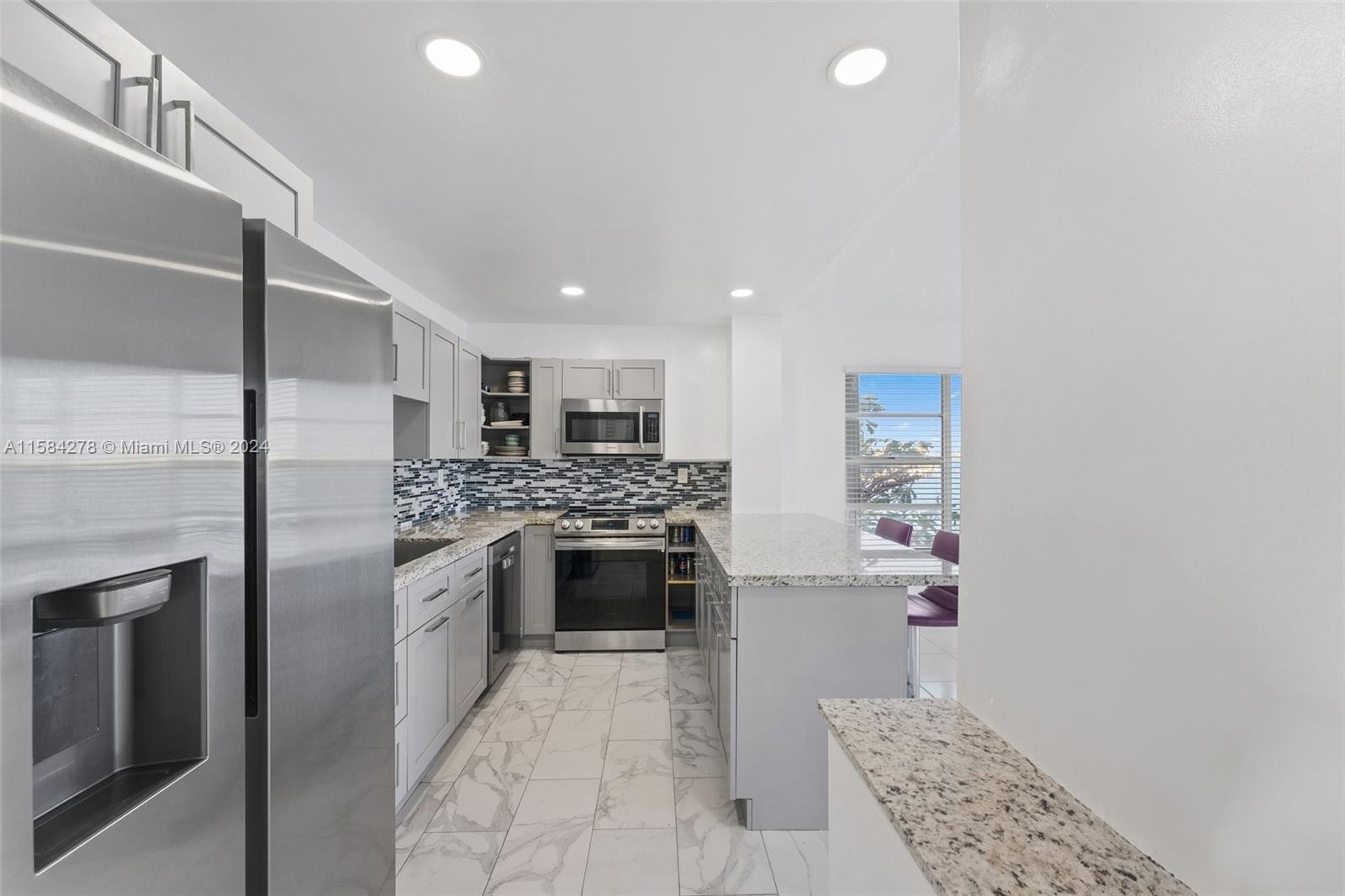 A kitchen features gray cabinets, granite countertops, stainless steel appliances, and white marble-look tile flooring — 11111 Biscayne Blvd # 3A, Miami FL 33181, MIAMI, FL