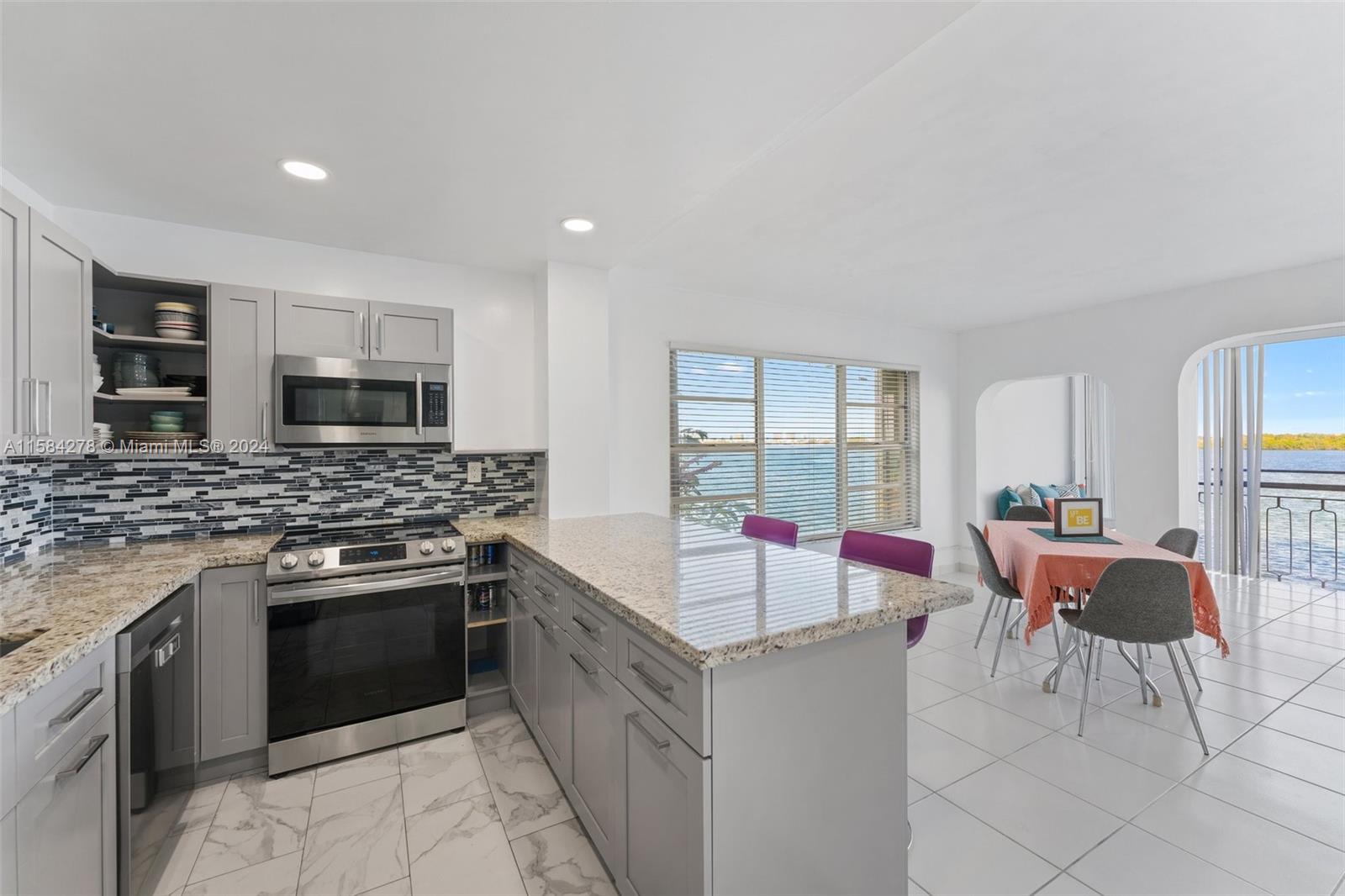 A kitchen with grey cabinets and granite countertops overlooks a dining area and water view — 11111 Biscayne Blvd # 3A, Miami FL 33181, MIAMI, FL