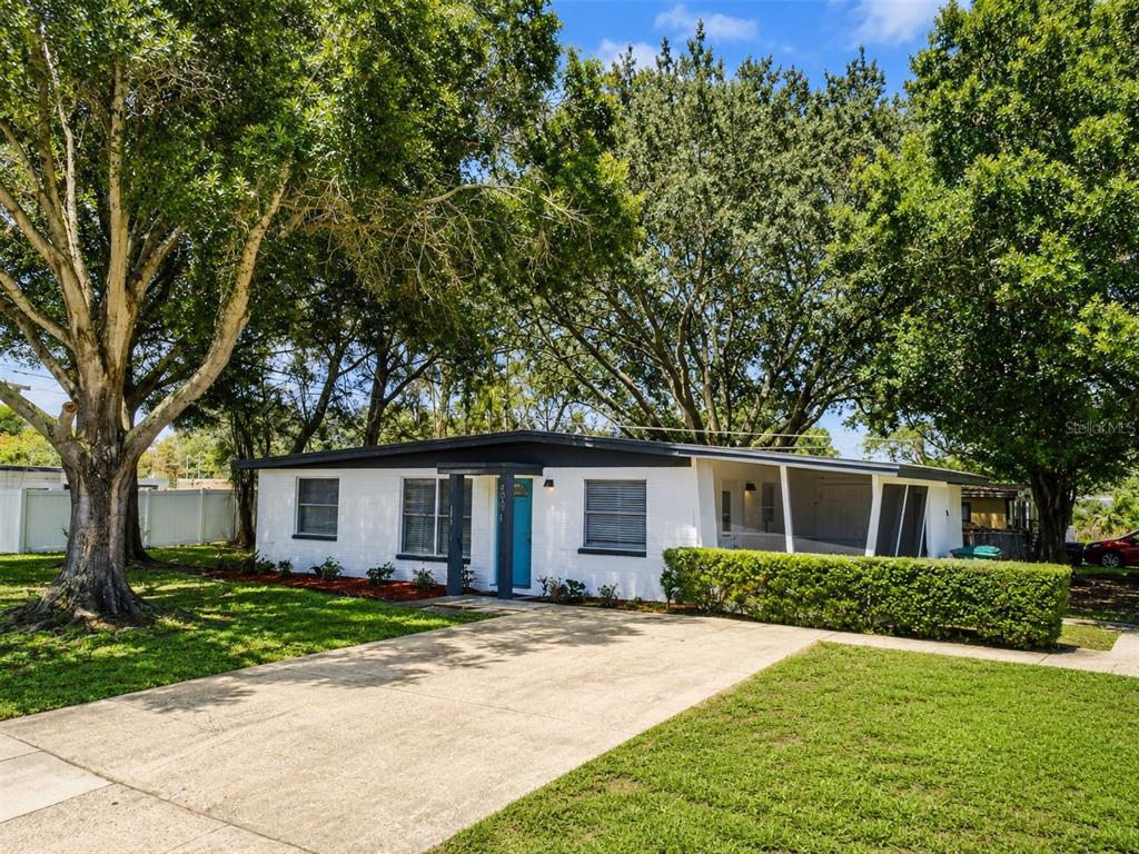 A single-story white brick house with a flat roof, blue front door, and large trees — 9001 82ND STREET, SEMINOLE, FL
