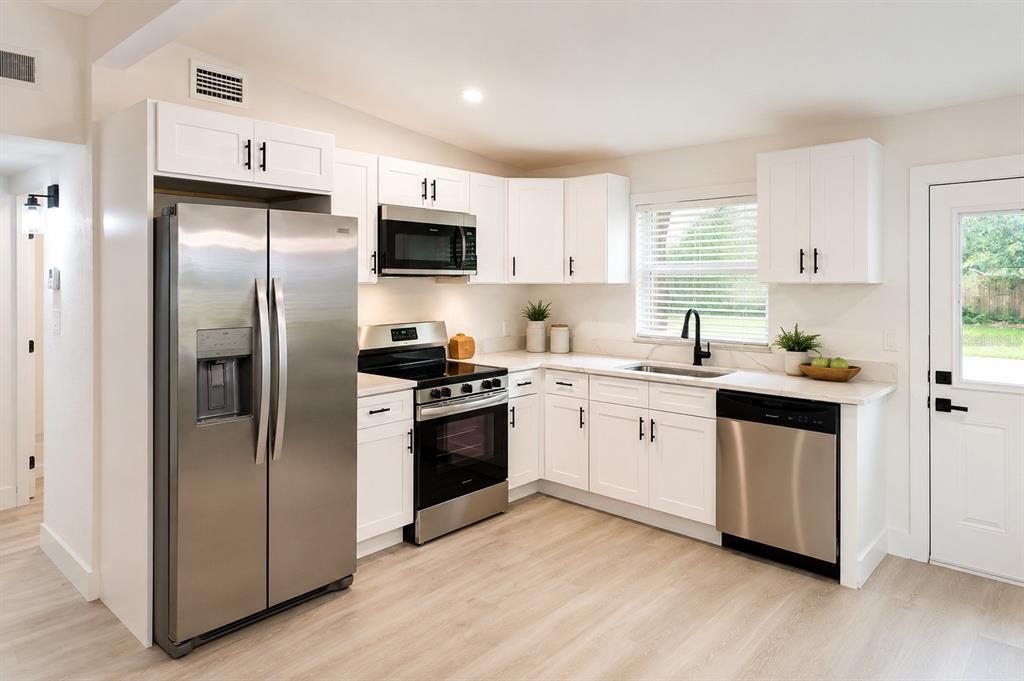 A kitchen features white cabinets, stainless steel appliances, light wood flooring, and a corner sink — 9001 82ND STREET, SEMINOLE, FL