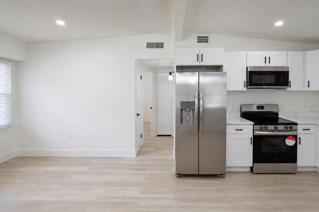 A kitchen features white cabinets, stainless steel appliances, and light-colored wood-look flooring — 9001 82ND STREET, SEMINOLE, FL