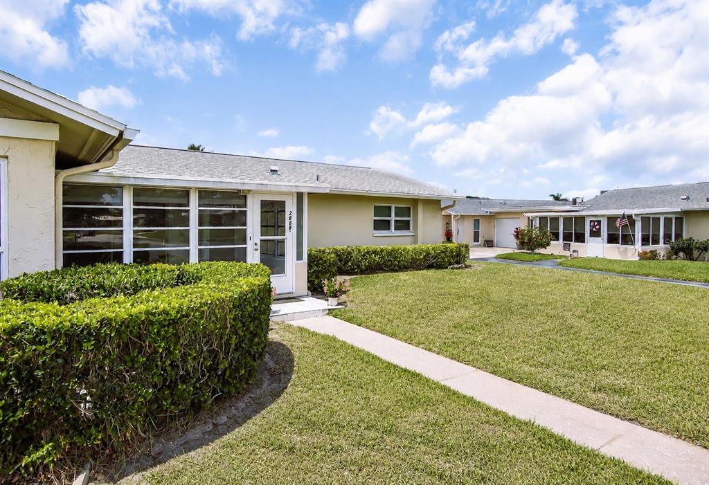 A single-story house with a light-colored exterior, a screened-in porch, and a manicured lawn — 2828 HIGHLANDS BOULEVARD UNIT A, PALM HARBOR, FL