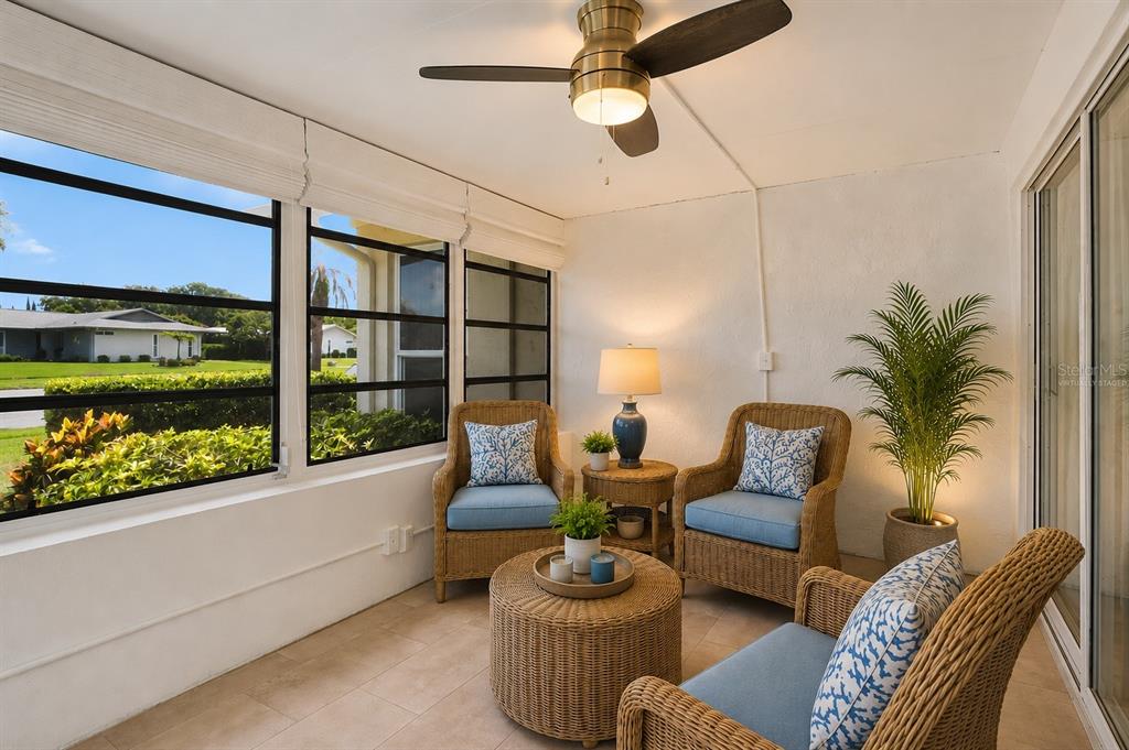 A sunroom features wicker furniture, a ceiling fan, and large windows overlooking a grassy yard — 2828 HIGHLANDS BOULEVARD UNIT A, PALM HARBOR, FL