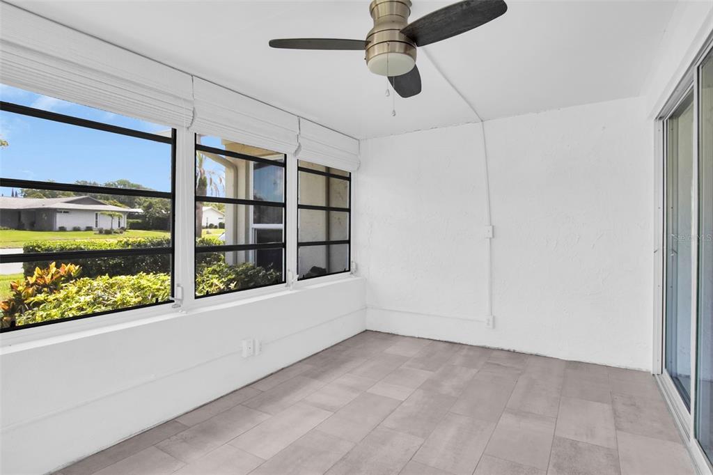 A sunroom with white walls, gray tile flooring, a ceiling fan, and large windows — 2828 HIGHLANDS BOULEVARD UNIT A, PALM HARBOR, FL