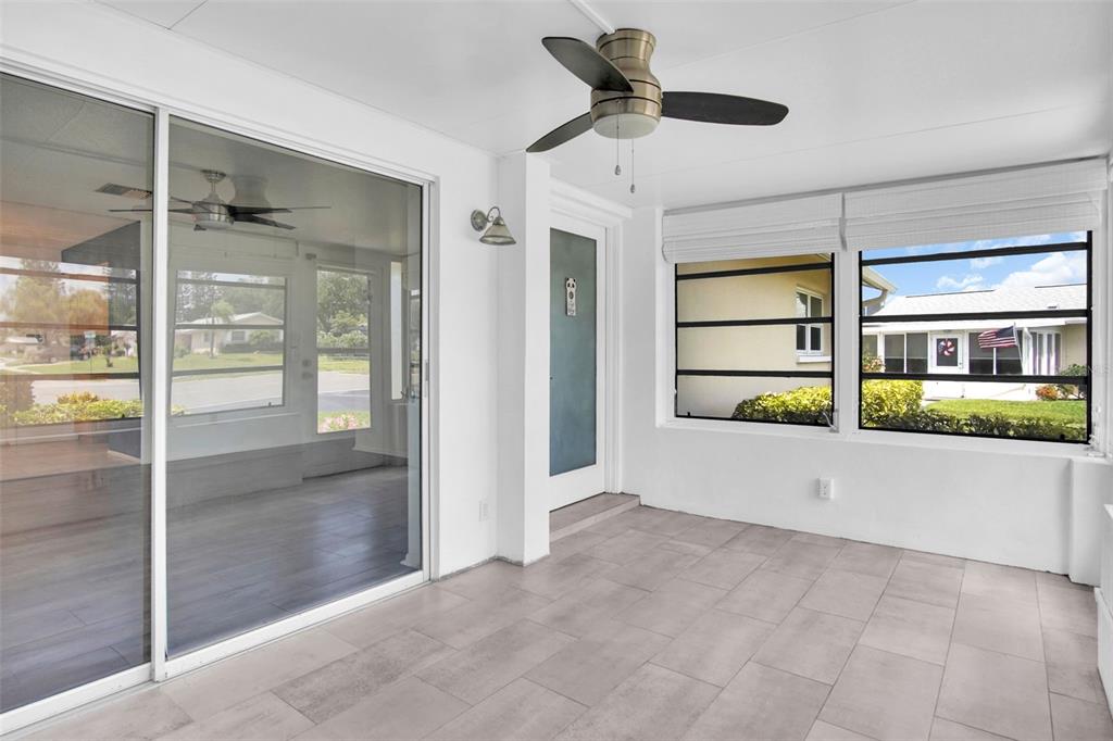 A sunroom with light tile flooring, a ceiling fan, and large windows overlooking a neighborhood — 2828 HIGHLANDS BOULEVARD UNIT A, PALM HARBOR, FL