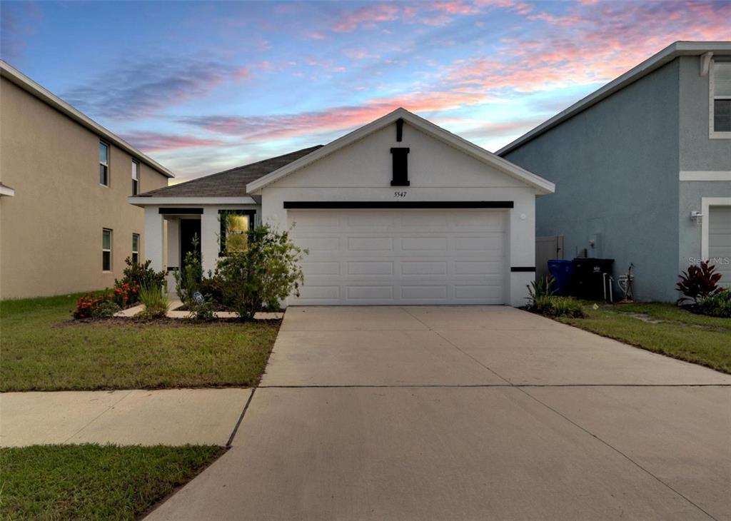 A single-story house with a white exterior, a two-car garage, and a concrete driveway — 5547 LOGAN CAVE AVENUE, WIMAUMA, FL
