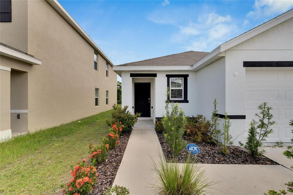 A white house with a black front door and a concrete walkway leading to the entrance — 5547 LOGAN CAVE AVENUE, WIMAUMA, FL