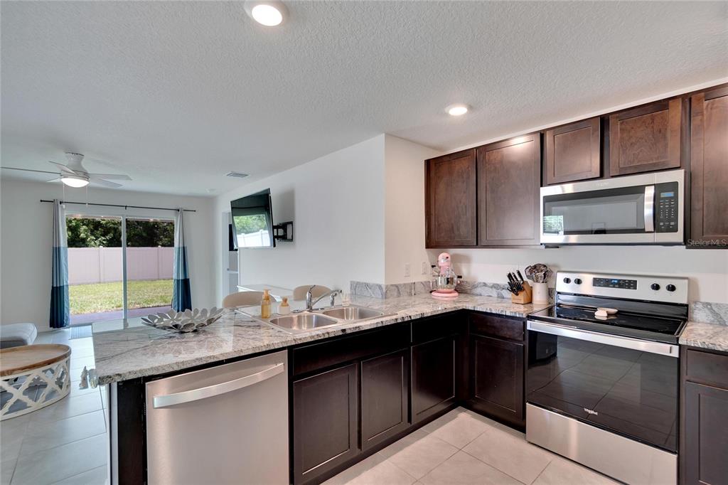A kitchen features dark wood cabinets, granite countertops, stainless steel appliances, and tile flooring — 5547 LOGAN CAVE AVENUE, WIMAUMA, FL