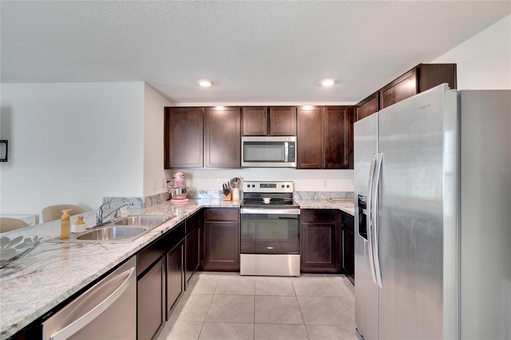 A kitchen with dark wood cabinets, stainless steel appliances, and granite countertops — 5547 LOGAN CAVE AVENUE, WIMAUMA, FL