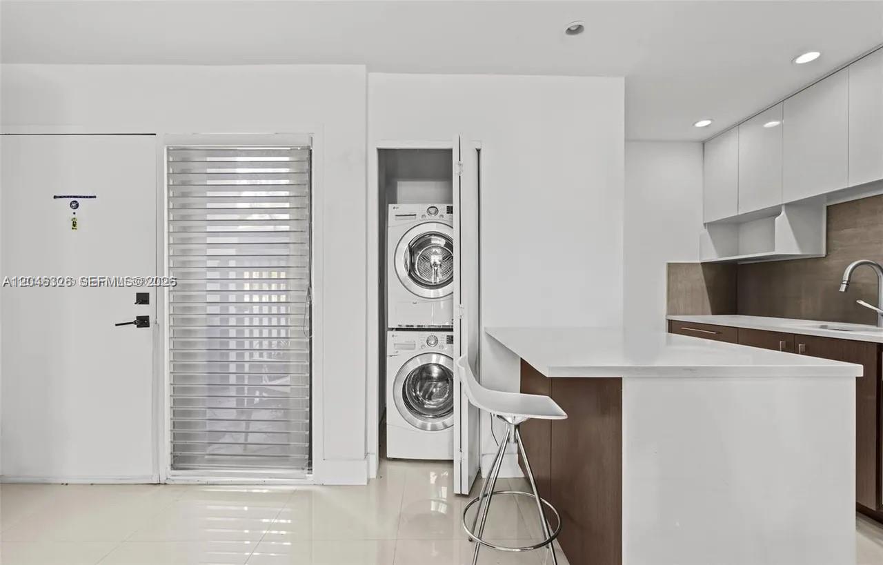A modern kitchen features white cabinetry, a breakfast bar, and a stacked laundry unit — 2715 Tigertail Ave # 102, Miami FL 33133, MIAMI, FL