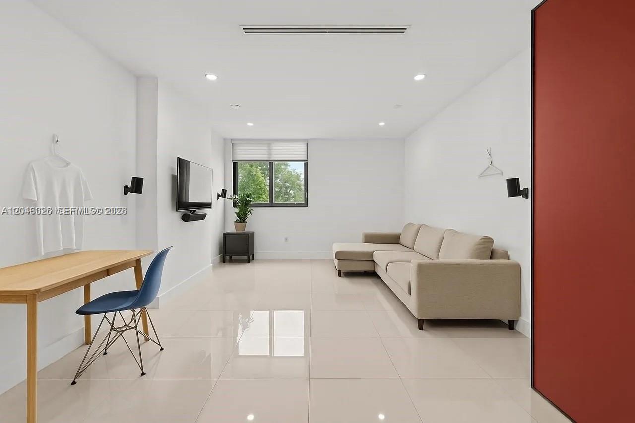 A minimalist living room features white walls, light tile flooring, a beige sectional, and desk — 2715 Tigertail Ave # 102, Miami FL 33133, MIAMI, FL