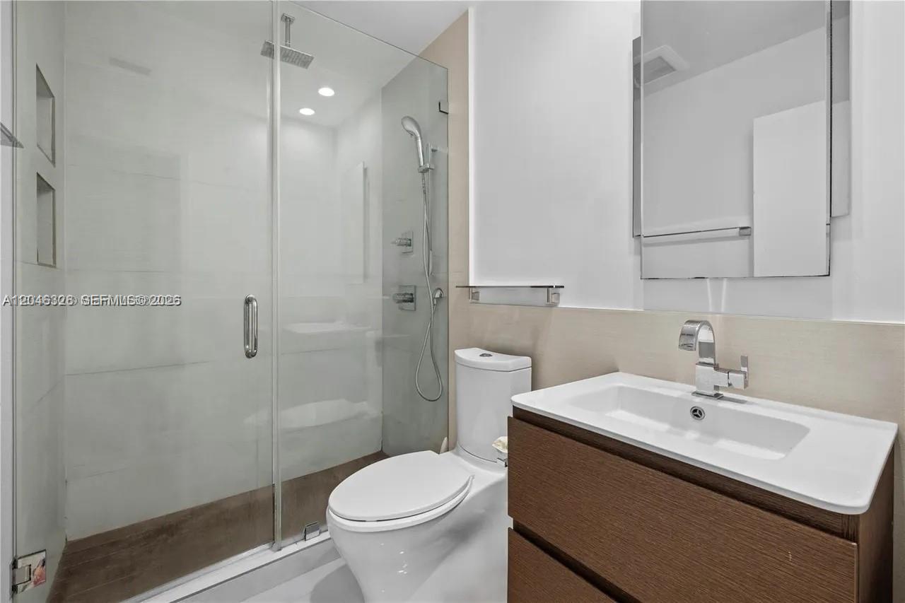 A modern bathroom features a glass-enclosed walk-in shower, a white toilet, and a wood vanity — 2715 Tigertail Ave # 102, Miami FL 33133, MIAMI, FL