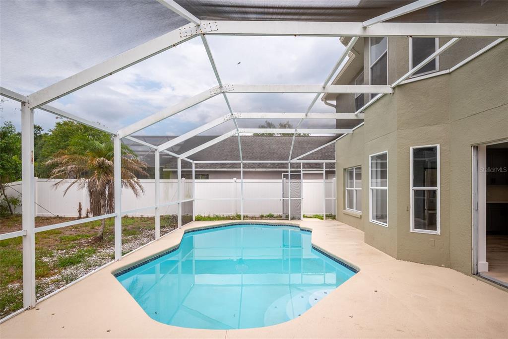 A swimming pool with a screened enclosure sits on a patio next to a house — 10224 MERRIMAC MANOR DRIVE, RIVERVIEW, FL