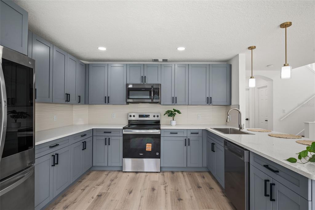 A kitchen features blue cabinets, stainless steel appliances, white countertops, and light wood flooring — 10224 MERRIMAC MANOR DRIVE, RIVERVIEW, FL