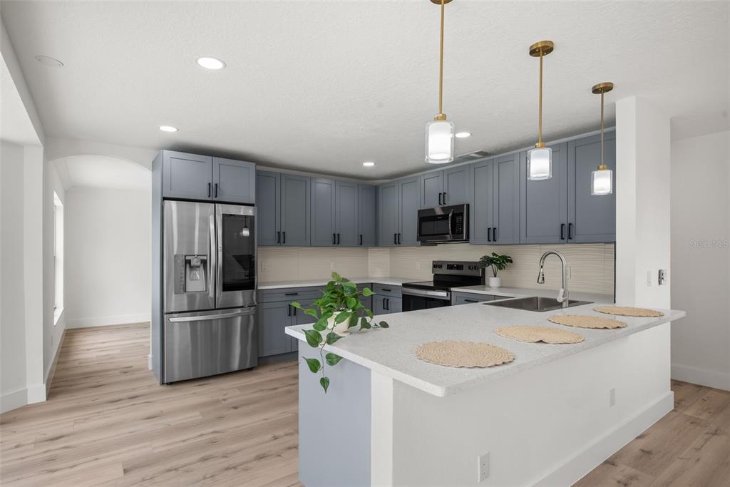 A kitchen features blue cabinets, stainless steel appliances, a white island, and light wood flooring — 10224 MERRIMAC MANOR DRIVE, RIVERVIEW, FL