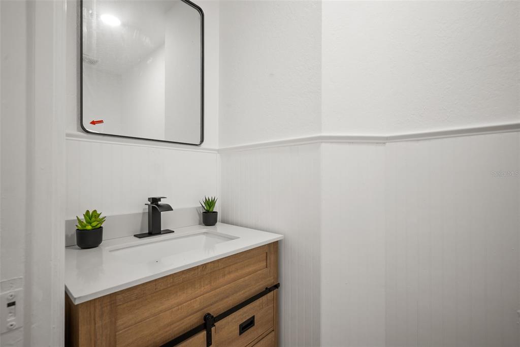 A bathroom features a wood vanity with a white countertop, black faucet, and wall mirror — 10224 MERRIMAC MANOR DRIVE, RIVERVIEW, FL