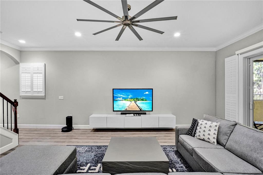 A living room features a wall-mounted television, a white media console, and gray sectional seating — 746 GRAND CYPRESS LANE, TARPON SPRINGS, FL