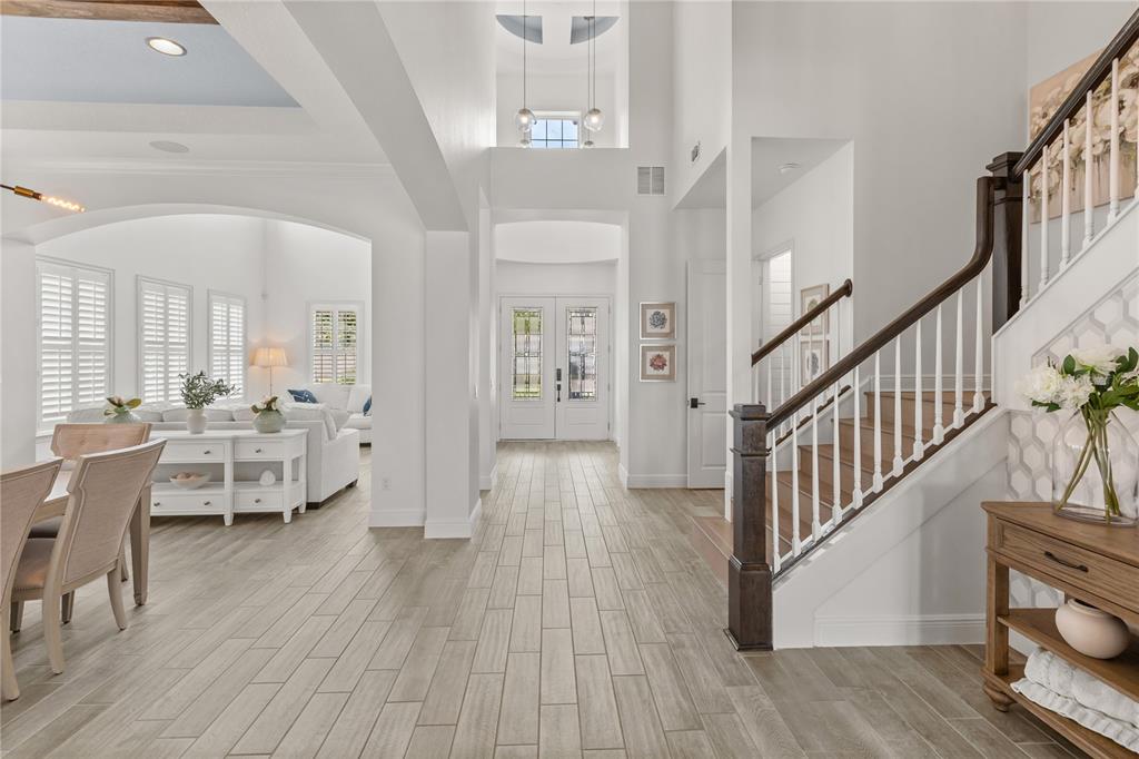 A bright foyer features wood-look tile flooring, a staircase with dark railings, and arched entryways — 15138 SHONAN GOLD DRIVE, WINTER GARDEN, FL