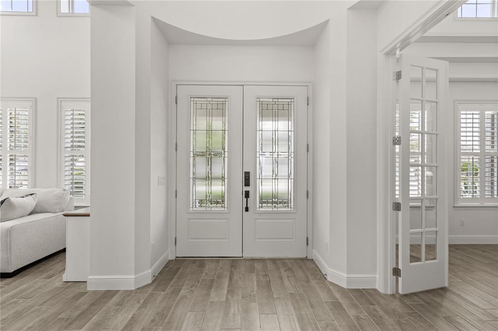 A bright entryway features double glass-paneled doors, white walls, and light wood-look tile flooring — 15138 SHONAN GOLD DRIVE, WINTER GARDEN, FL