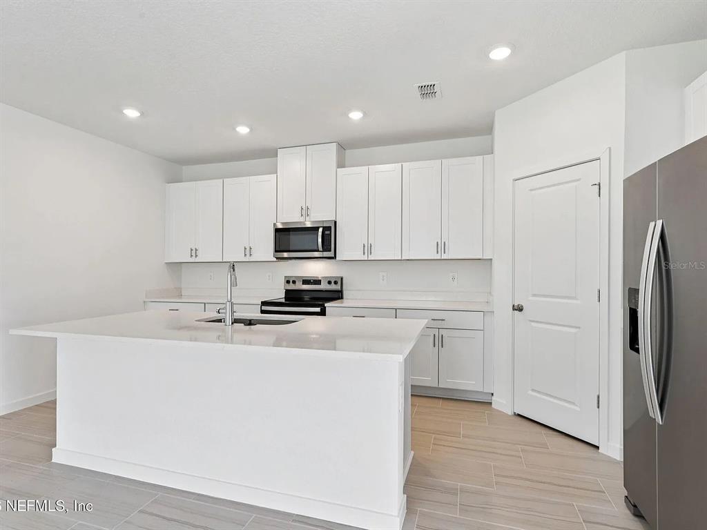A modern kitchen features white cabinets, a central island with a sink, and stainless appliances — 59 ARARAT DRIVE, PALM COAST, FL
