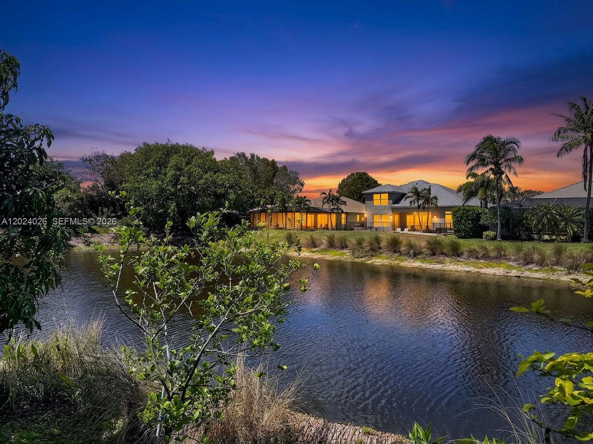 A two-story house with a screened patio sits behind a pond at sunset — NAPLES, FL
