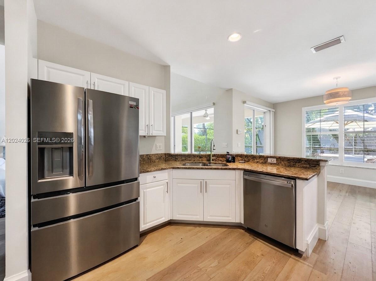 A kitchen features stainless steel appliances, white cabinetry, and granite countertops over light wood flooring — NAPLES, FL