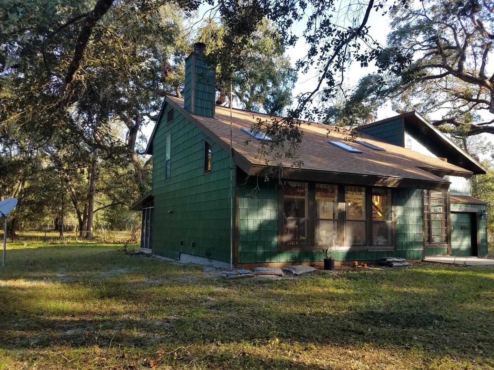 A green-sided house with a chimney and skylights sits on a grassy, tree-shaded lot — 1588 Cr 652a, FL 33513, FL