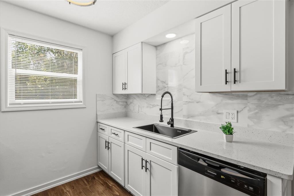A kitchen features white cabinets, marble-look backsplash, a stainless steel sink, and a dishwasher — 22632 SE HAWTHORNE ROAD, HAWTHORNE, FL