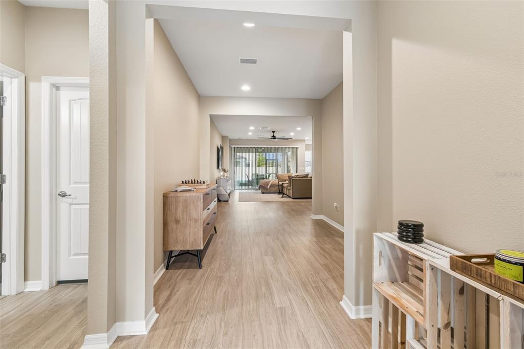 A hallway with light wood-look flooring leads toward a living area with sliding glass doors — 8012 OLIVE BROOK DRIVE, WESLEY CHAPEL, FL