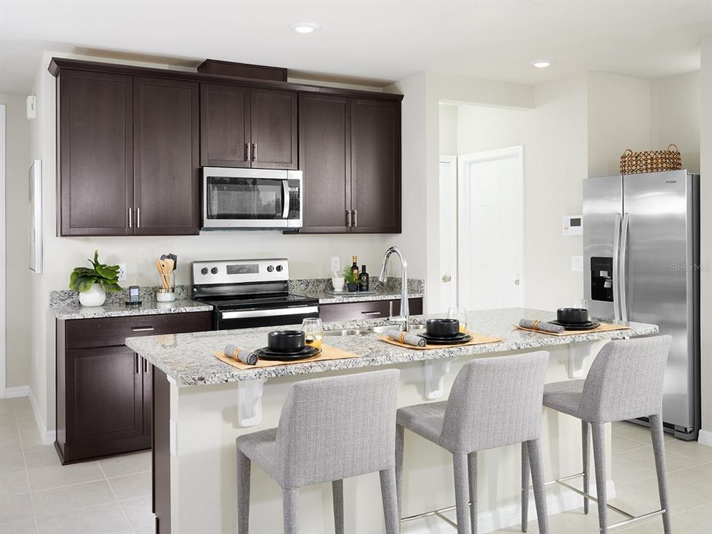 A kitchen features dark wood cabinets, granite countertops, a stainless steel island, and three chairs — 4539 RANGELAND WAY, ST CLOUD, FL