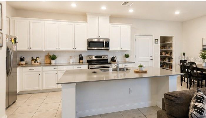 A modern kitchen features white cabinetry, a large center island, and stainless steel appliances — 3890 KNOTTY PINE STREET, ST CLOUD, FL