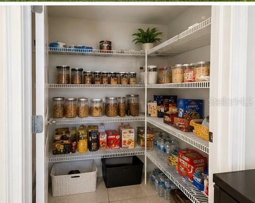 A pantry features white wire shelving stocked with various food containers, jars, and bottled water — 3890 KNOTTY PINE STREET, ST CLOUD, FL