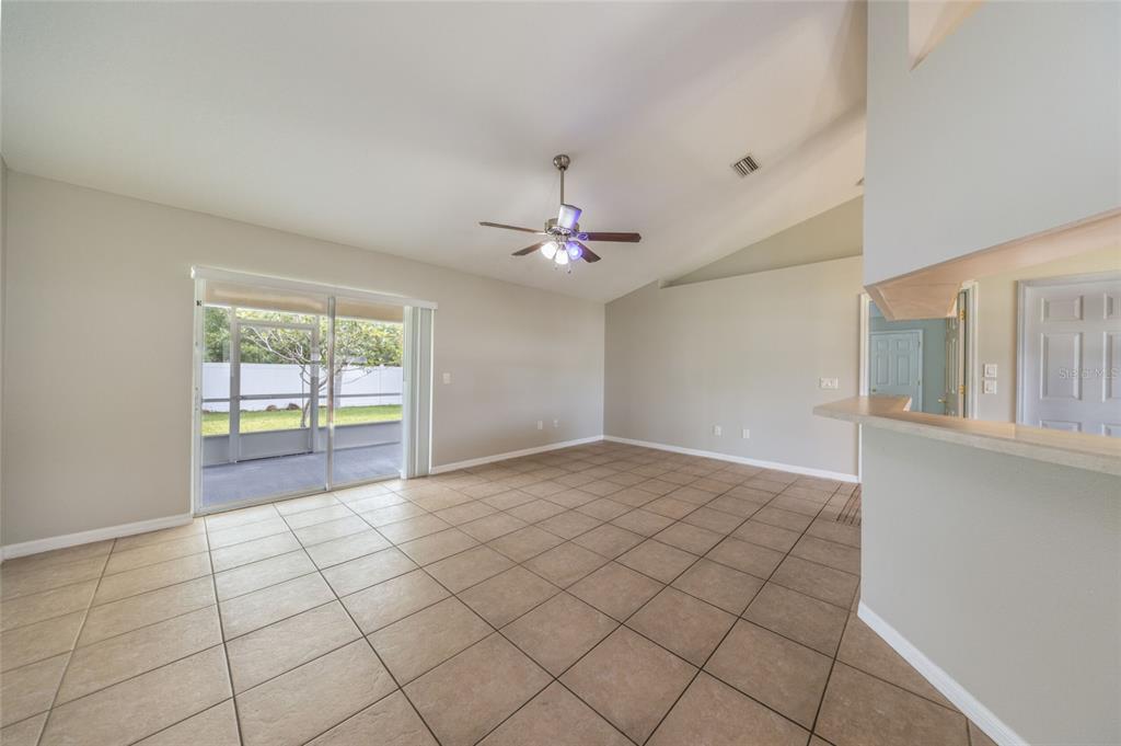 A living room with beige tile flooring, a vaulted ceiling, a ceiling fan, and sliding doors — 37 ROCKEFELLER DRIVE, PALM COAST, FL