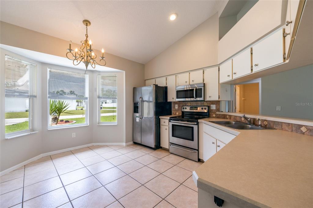 A kitchen with white cabinets, stainless steel appliances, tile flooring, and a breakfast nook area — 37 ROCKEFELLER DRIVE, PALM COAST, FL