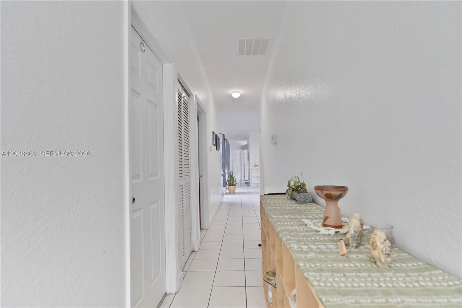 A long, white-walled hallway features tiled flooring, several closed doors, and a wooden storage unit — 249 SE 32nd Ave, Homestead FL 33033, HOMESTEAD, FL