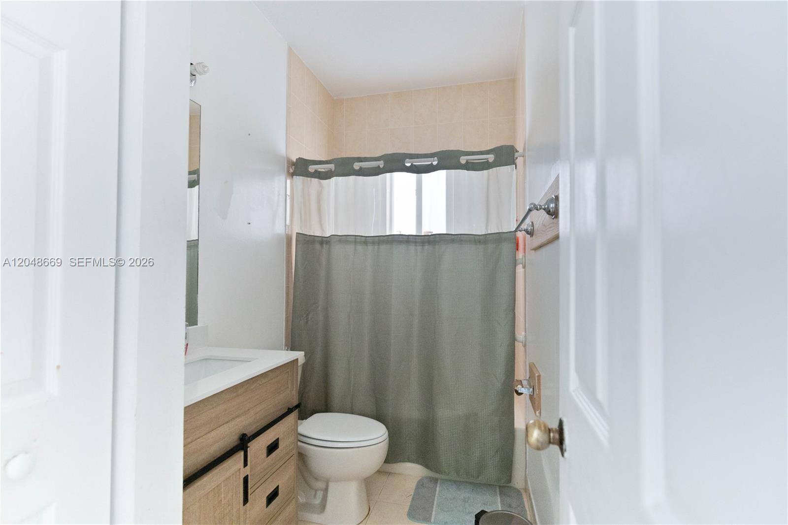 A bathroom features a wood-toned vanity, a white toilet, and a shower with a curtain — 249 SE 32nd Ave, Homestead FL 33033, HOMESTEAD, FL