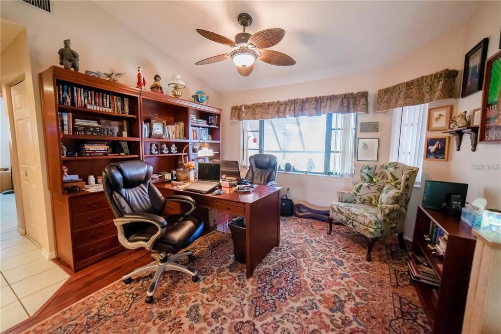 A home office features a wooden desk, a leather chair, built-in bookshelves, and patterned carpeting — 145 BUNKER ROAD, ROTONDA WEST, FL