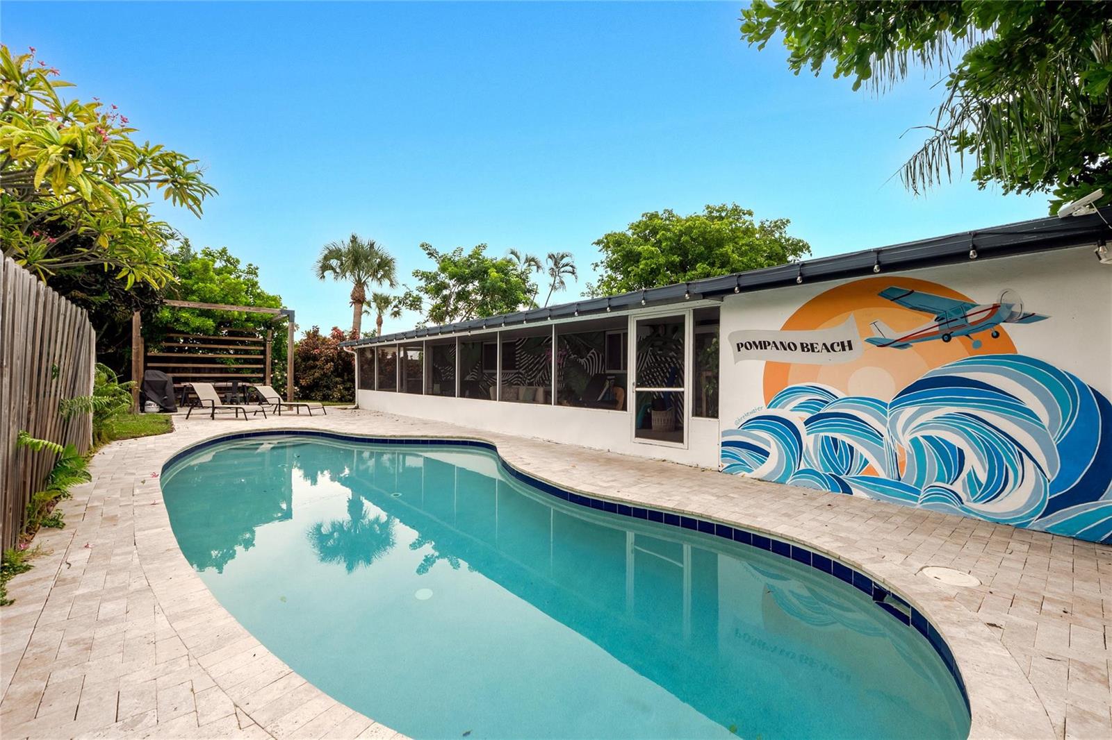 A backyard swimming pool sits next to a house wall featuring a Pompano Beach mural — 2621 NE 20th Street, Pompano Beach FL 33064, POMPANO BEACH, FL