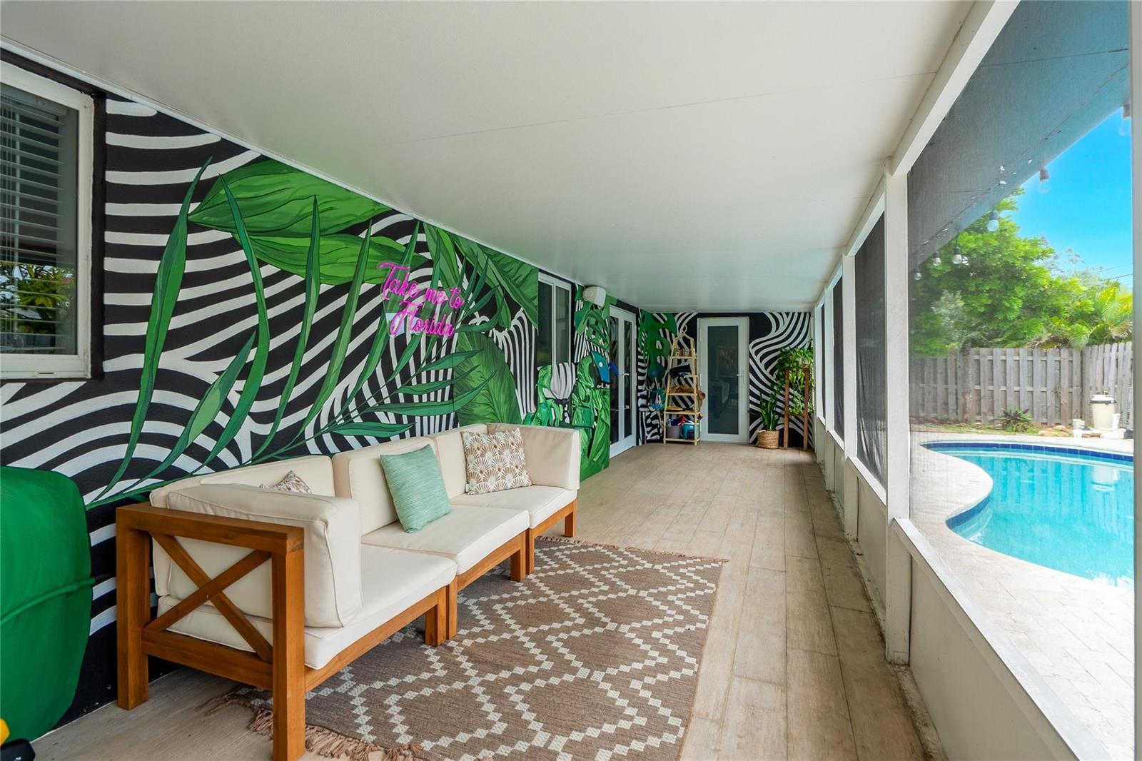 A screened-in patio features a tropical mural, a beige sofa, and a view of a pool — 2621 NE 20th Street, Pompano Beach FL 33064, POMPANO BEACH, FL