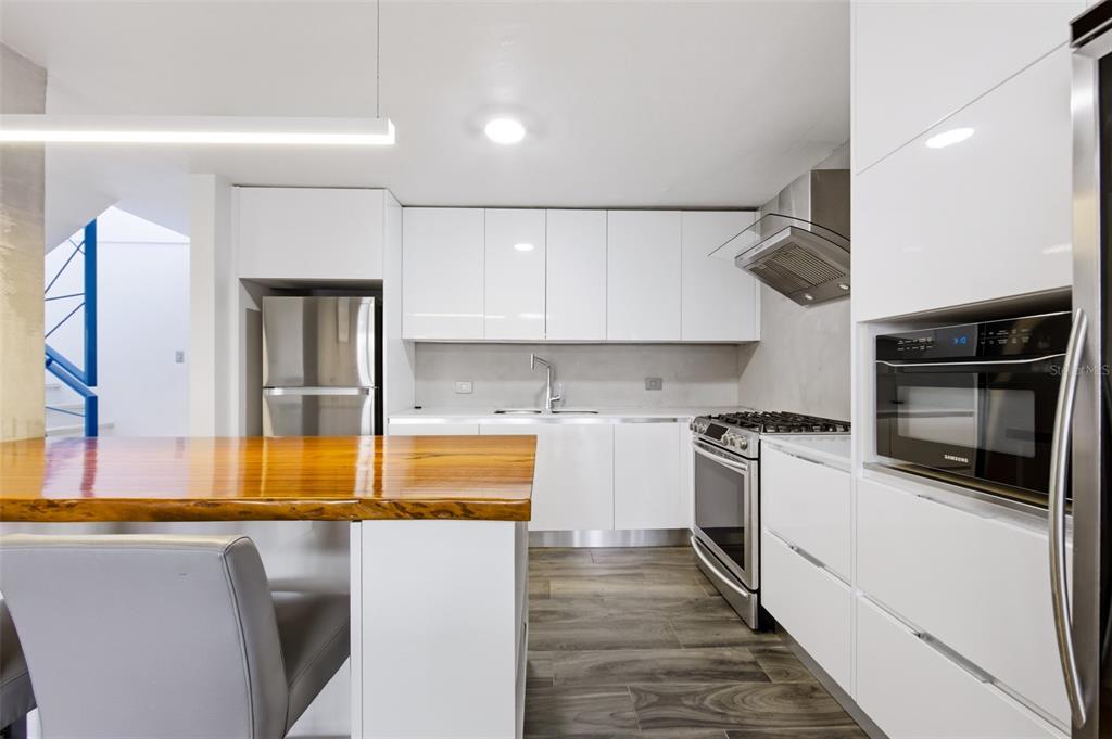 A modern kitchen features white cabinets, stainless steel appliances, and a wooden breakfast bar — K4 COSTA DORADA UNIT 58, DORADO, PR