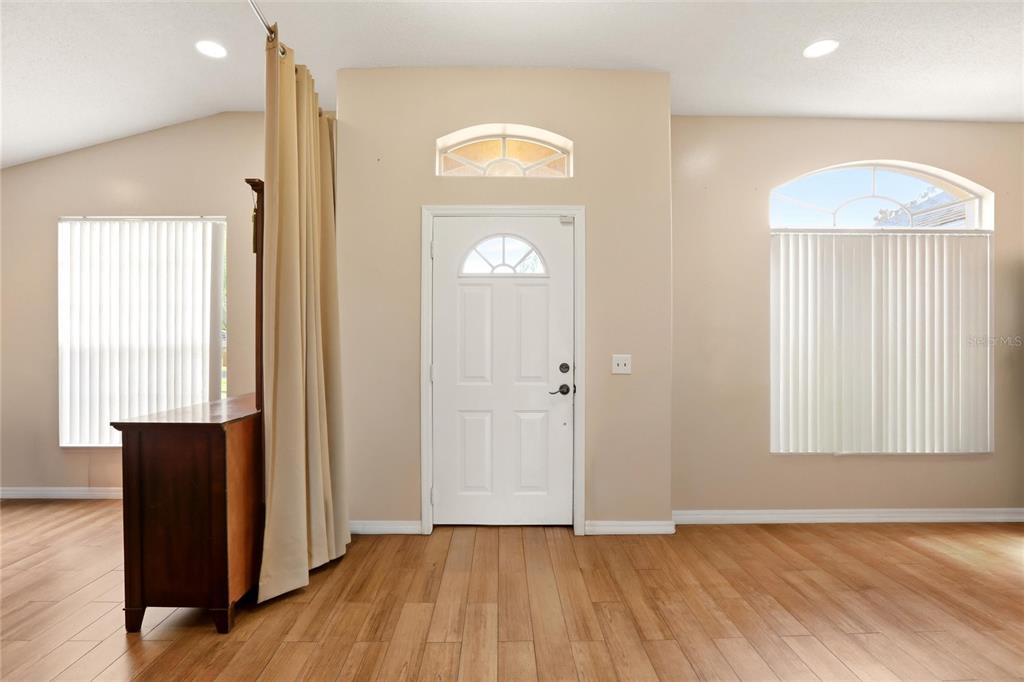 An entryway features light wood flooring, a white front door, and a beige curtain divider — 3535 BEAU CHENE DRIVE, KISSIMMEE, FL