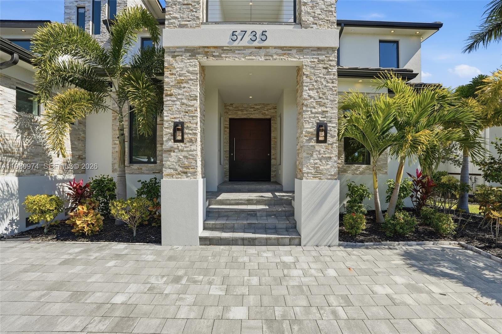 The exterior of a modern house features stone cladding, a dark front door, and palm trees — 5735 Riverside Dr, Cape Coral FL 33904, CAPE CORAL, FL