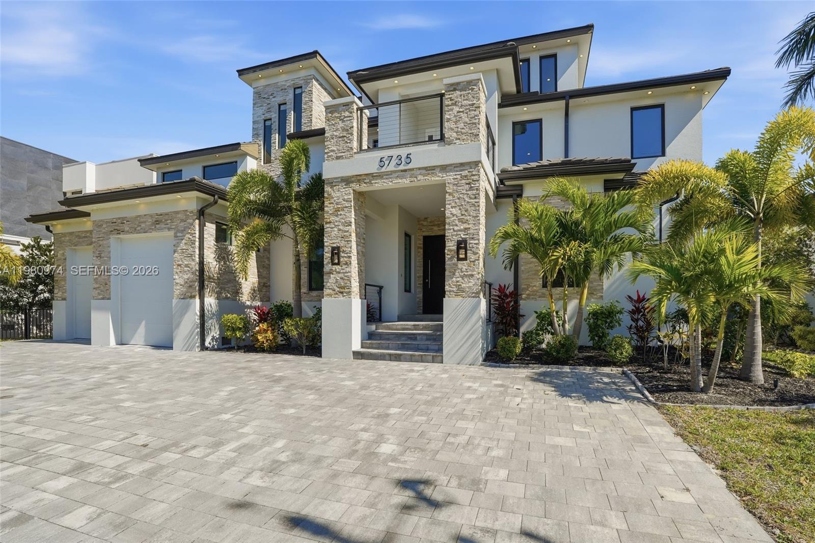 A modern two-story house features stone veneer accents, a paved driveway, and palm trees — 5735 Riverside Dr, Cape Coral FL 33904, CAPE CORAL, FL