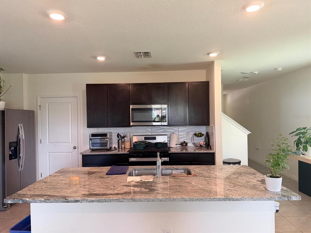A kitchen features dark wood cabinets, granite countertops, a center island, and stainless steel appliances — 35665 SUNFLOWER HILL DRIVE, ZEPHYRHILLS, FL