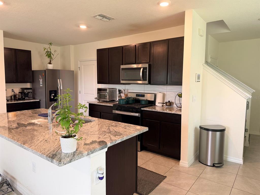 A kitchen features dark wood cabinets, granite countertops, a center island, and stainless steel appliances — 35665 SUNFLOWER HILL DRIVE, ZEPHYRHILLS, FL