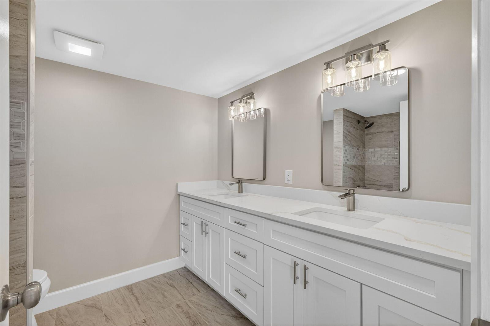 A modern bathroom features a white double vanity, marble countertop, and two framed mirrors — 100 Waterway Road # A304, Tequesta FL 33469, TEQUESTA, FL