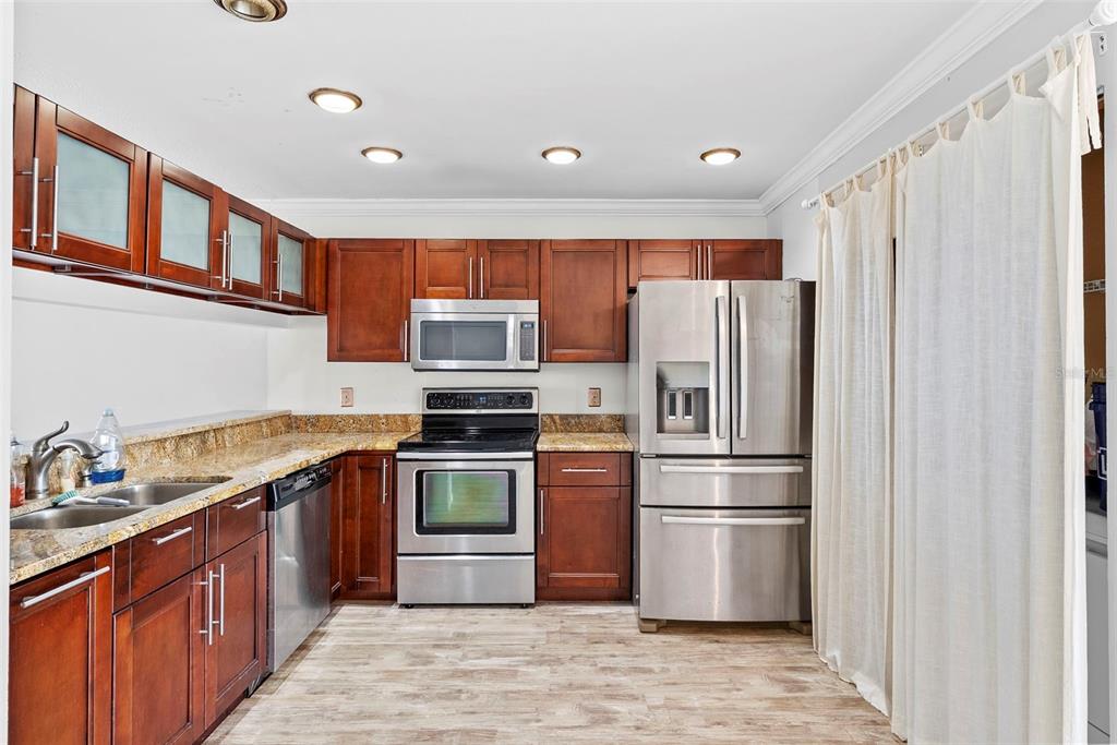A kitchen features dark wood cabinets, stainless steel appliances, granite countertops, and light wood flooring — 5314 ABINGER COURT, TAMPA, FL