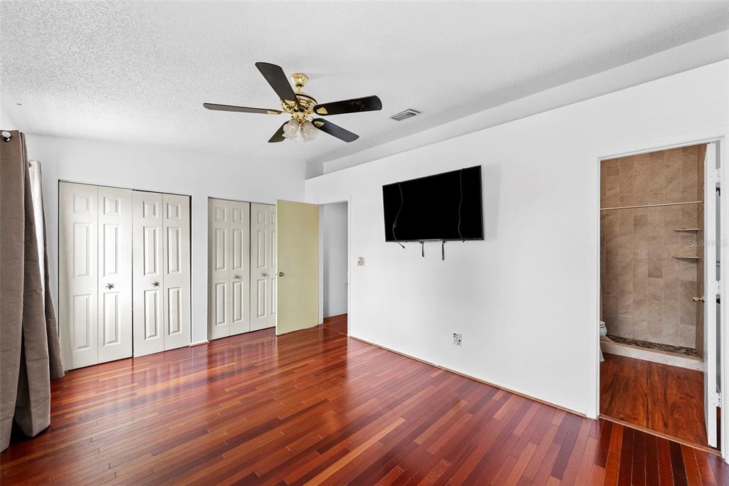 A bedroom with hardwood floors, a ceiling fan, a wall-mounted television, and an attached bathroom — 5314 ABINGER COURT, TAMPA, FL